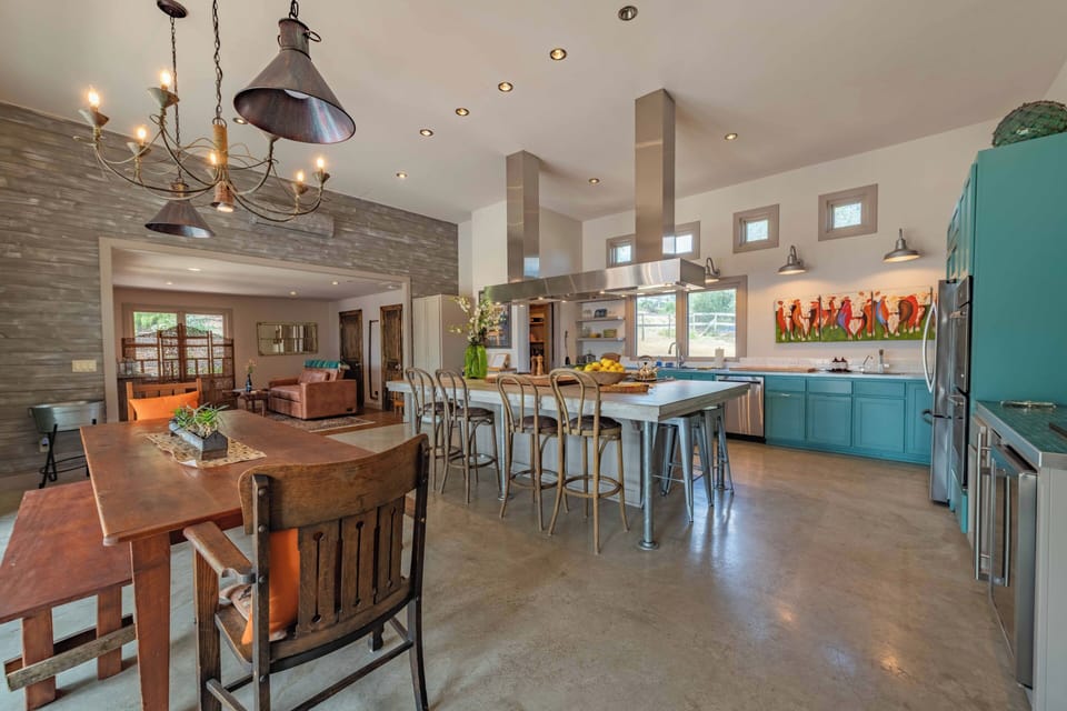 Gather around the spacious kitchen island with friends and family. Turquoise cabinets, stainless steel appliances, and open shelving create a vibrant, welcoming space for cooking and entertaining together.