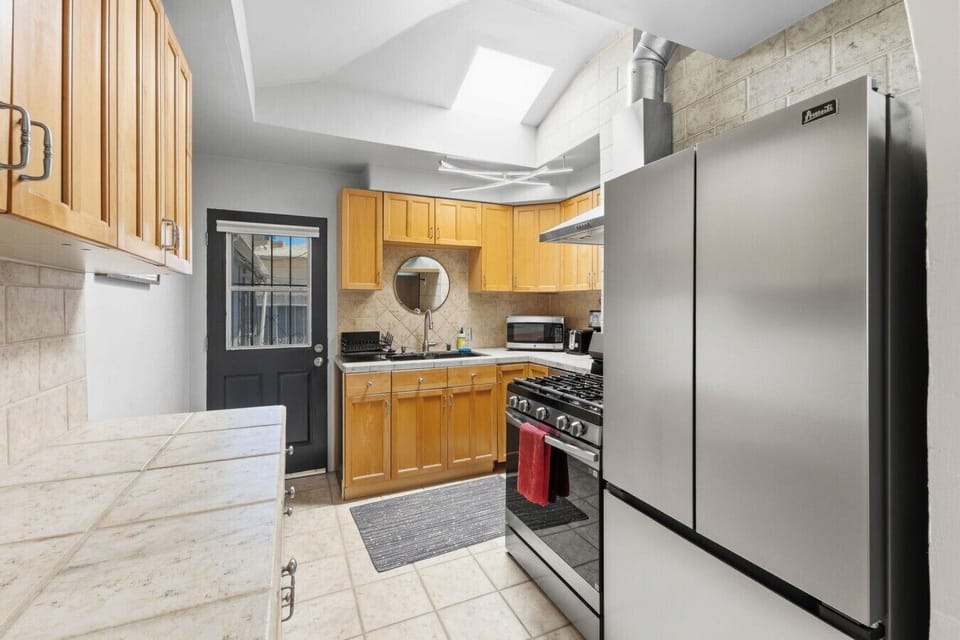 Bright kitchen featuring a large double-door stainless steel refrigerator, gas stove, and overhead skylight for natural light.