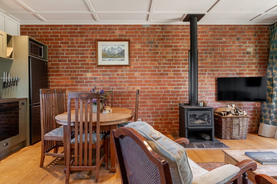 Open-plan living and dining with exposed brick, wood fire, and rich textures - a warm welcome after exploring Clyde and Alexandra.