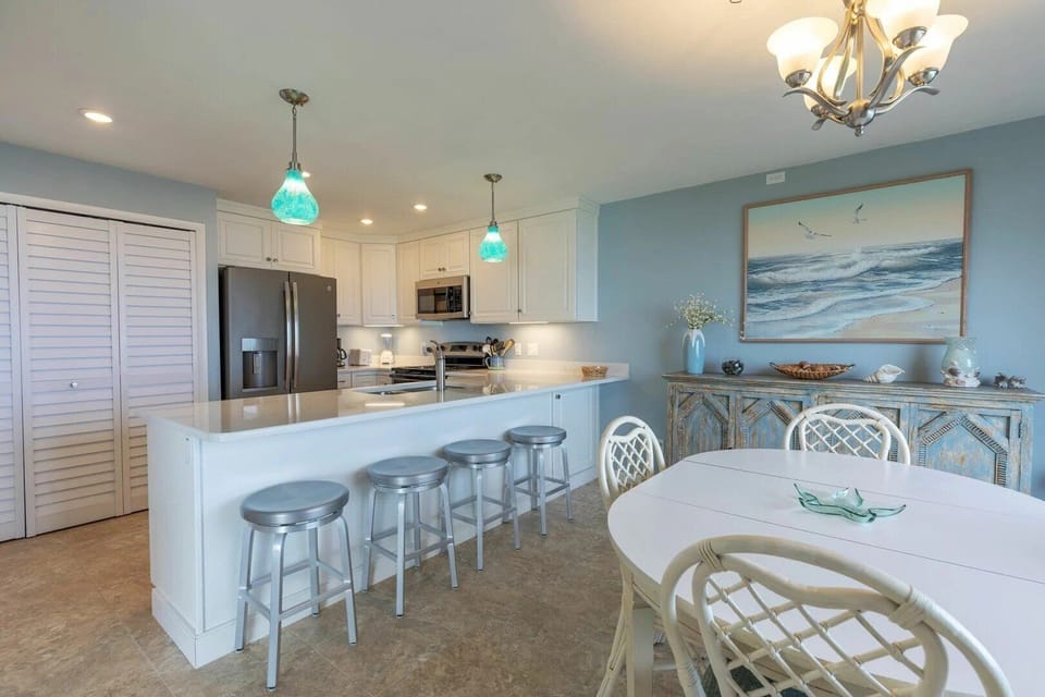 Enjoy a bright, beach-inspired kitchen and dining area with modern appliances, seating for the whole family, and coastal décor—perfect for gathering after a day of sun and surf.