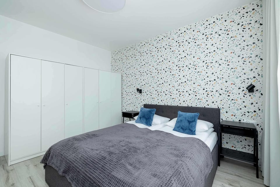 Another angle of the bedroom showing the bed, blue cushions, and a wardrobe. The walls feature decorative wallpaper.