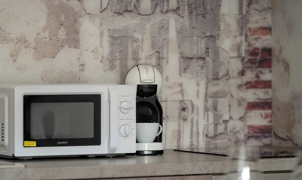 A kitchen counter featuring a microwave and capsule coffee machine. The brick-style backsplash adds a rustic charm.