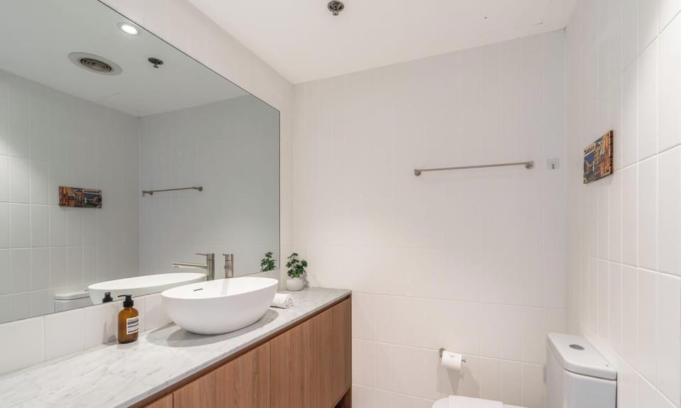 A clean and bright bathroom interior, featuring a modern vessel sink, expansive mirror, and neutral-toned finishes.