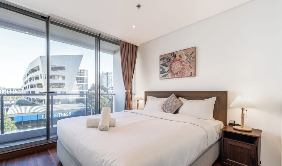 A comfortable bedroom with a view of the outside through a large floor-to-ceiling window.