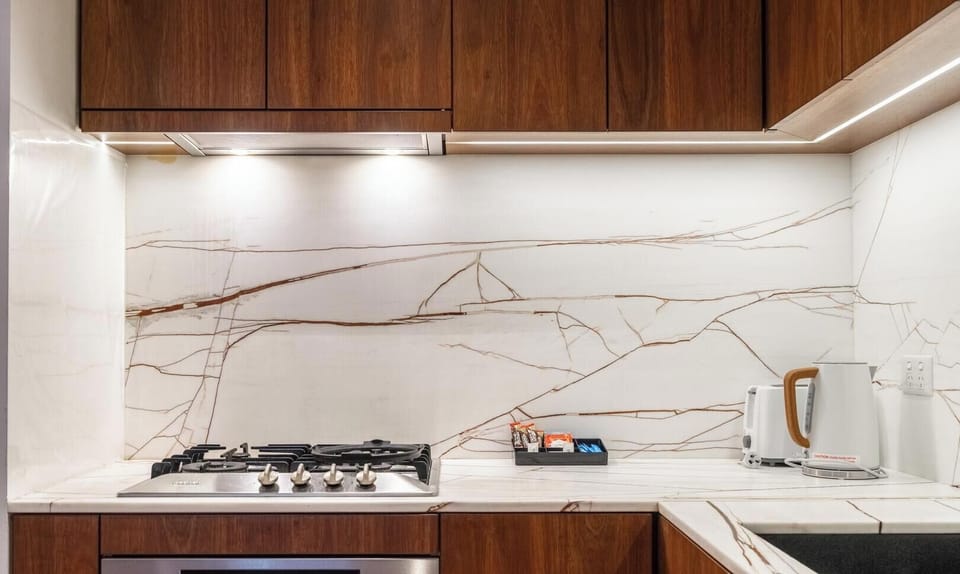 A modern kitchen featuring dark cabinetry and marble-patterned wall tiling.