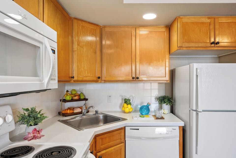 Kitchen with wooden cabinets, white microwave, refrigerator, dishwasher, and electric stove, countertop decorated with fruit and flowers creating a welcoming cooking space.