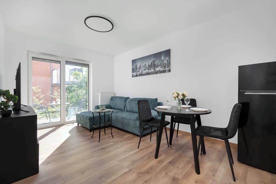 A bright living area with a sofa, dining table, and wide windows. The setup feels open and inviting.