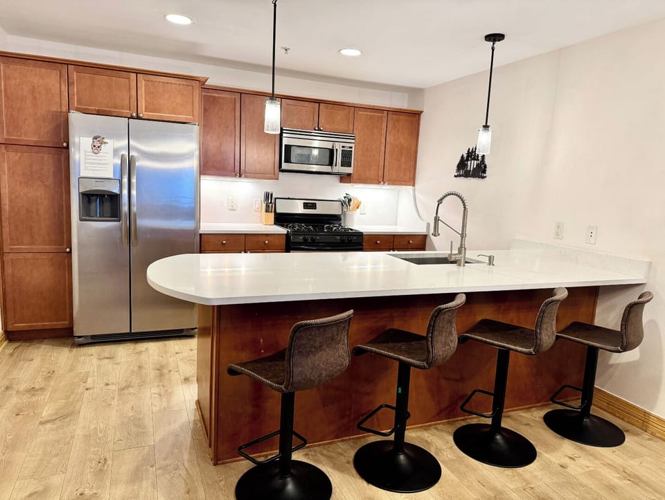 Your fully equipped kitchen features rich wood cabinetry, stainless steel appliances, and a spacious island with seating—perfect for preparing meals and gathering together.