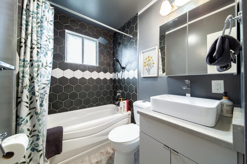 Freshen up in the upstairs bathroom with a tub & shower, black hex tile, a vessel sink, a mirrored cabinet & a towel hook.