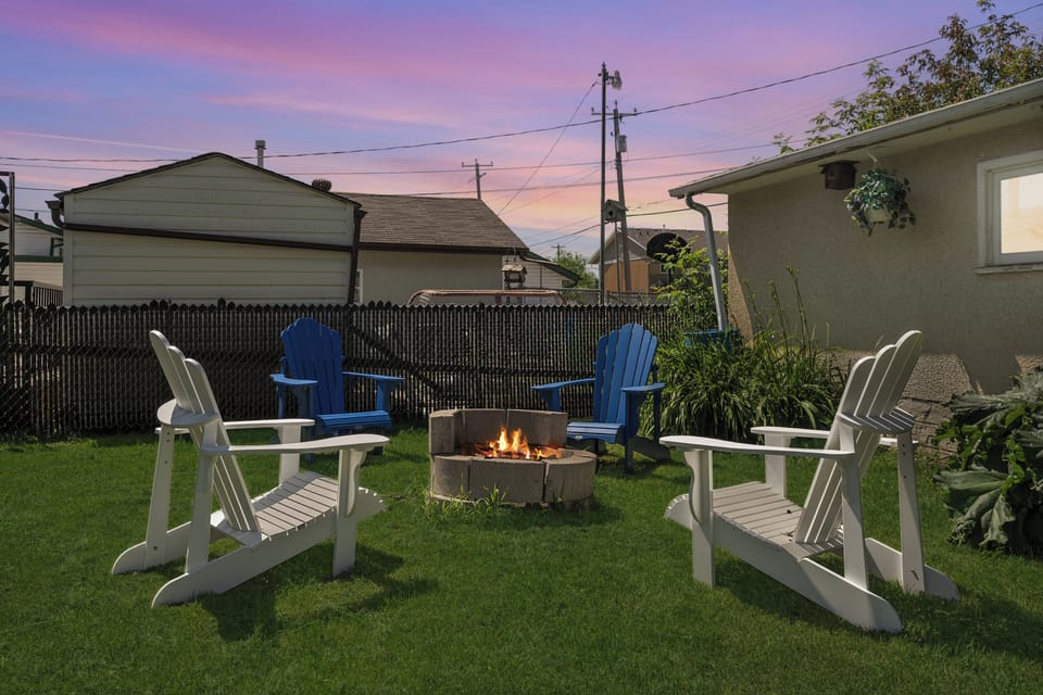 Light the fire pit on a summer evening, with Adirondack chairs set around it on the lawn of the fully fenced backyard.