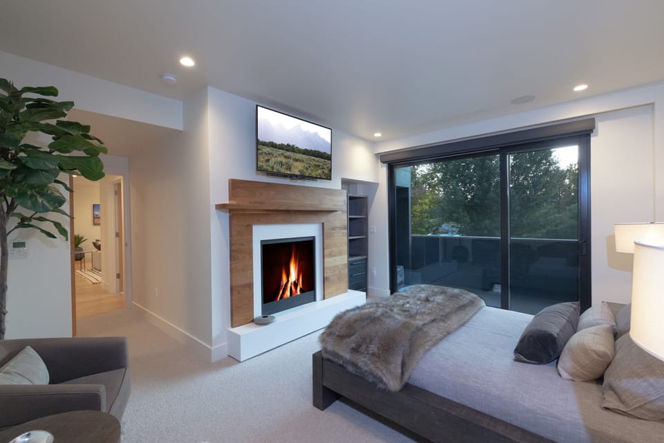 Unwind in your luxurious bedroom sanctuary, where a crackling fireplace and modern TV create the perfect ambiance for cozy evenings. Wake up to garden views through floor-to-ceiling windows.