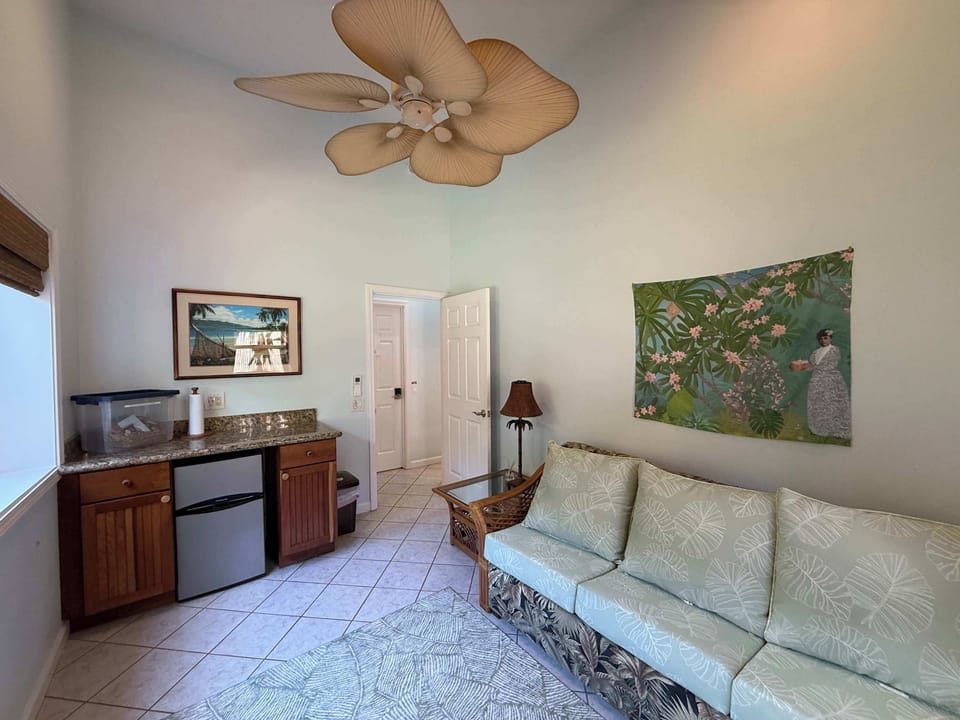
Royal Suite Living Room & Kitchenette. Comfort of AC, ceiling fan, convenient in-room coffee and snacks provided. Relax in your private living room, watch shows on the smart TV or look out into the lush tropical gardens.