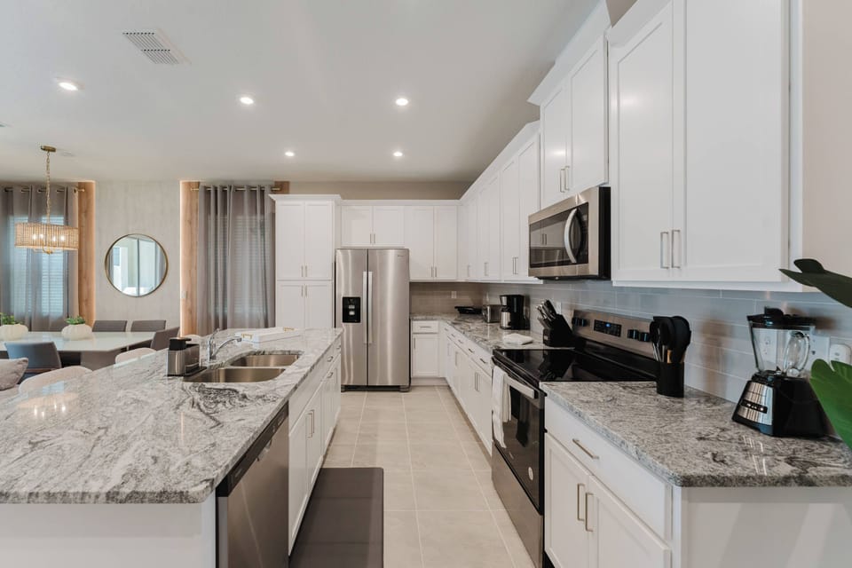 This sleek kitchen features elegant white cabinetry and granite countertops, creating a bright cooking space. Modern stainless steel appliances complement the design, and natural light enhances your culinary experience.