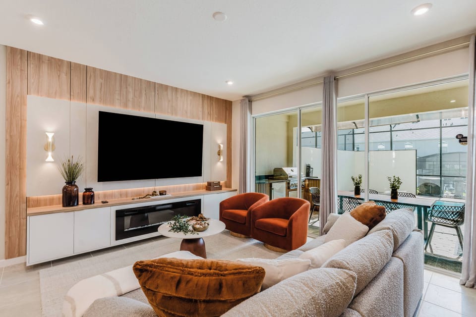Enjoy the natural light pouring through the large glass doors in this stylish living area, complete with a cozy neutral sofa and bold terracotta armchairs, all enhanced by a warm wood accent wall that complements the modern decor.
