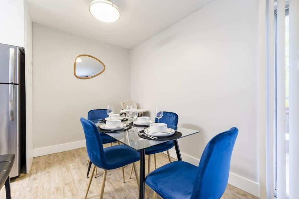 Dine in style with seating for four on elegant blue velvet chairs around a sleek glass table, next to natural light from sliding doors