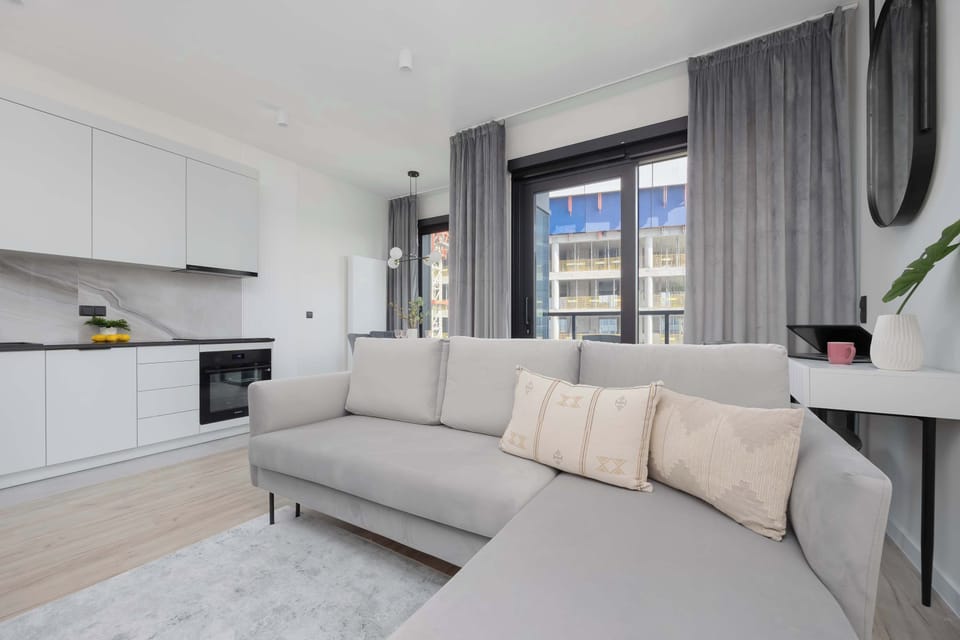 The bright living room with large windows fills the interior with natural light and opens up to the city.