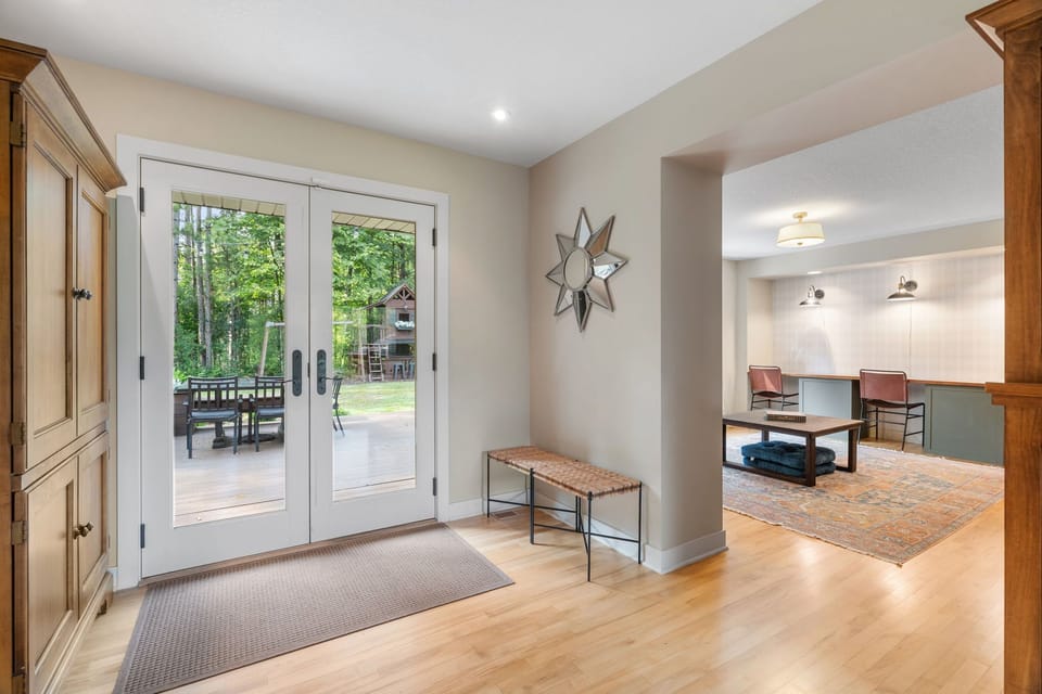 Step into your welcoming entrance where glass doors reveal stunning forest views and warm wood accents create an inviting home away from home.