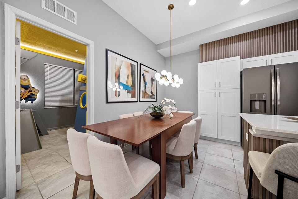 This bright and stylish dining area boasts a sleek wooden table with plush upholstered chairs, ensuring a comfortable atmosphere for meals. Eye-catching art and modern lighting enhance the warm ambiance for an inviting experience.