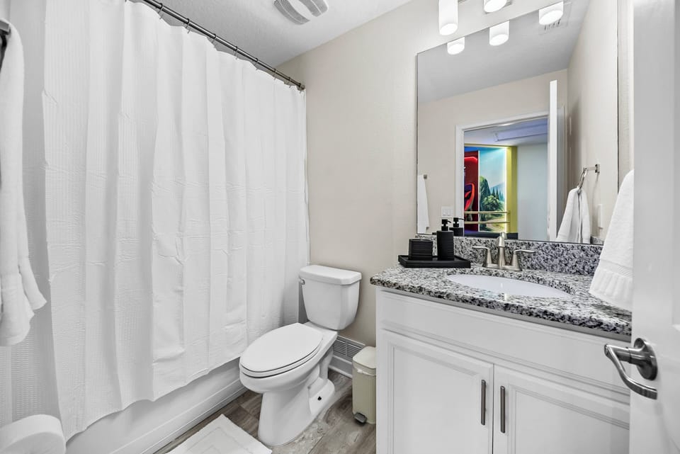 This bright bathroom boasts a sleek granite countertop and stylish fixtures. Fresh white curtains enhance the ambiance, while thoughtful decor adds convenience, making it a perfect space for your comfort.
