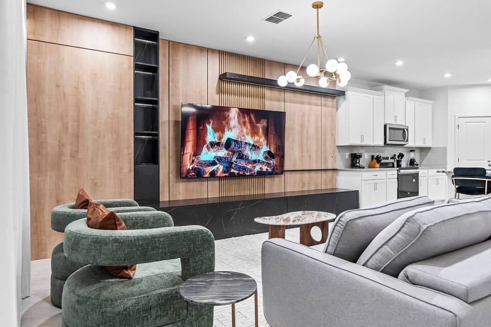 Relax in the cozy ambiance of this inviting living area, complete with a sleek fireplace, warm wood paneling, plush green accent chairs, and a soft gray sofa for a chic and comfortable atmosphere.