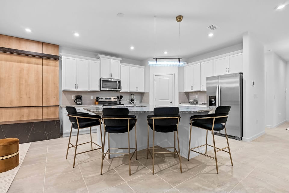 Welcome to a bright, modern kitchen with sleek white cabinetry and a beautiful marble countertop. The stylish bar stools create a sophisticated atmosphere, ideal for enjoying morning coffee or evening chats.