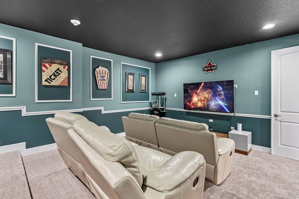 Welcome to this cozy entertainment room, where plush cream sofas invite you to unwind and enjoy a movie on the large flat-screen TV, all set against playful teal walls adorned with vintage film posters for a vibrant touch.