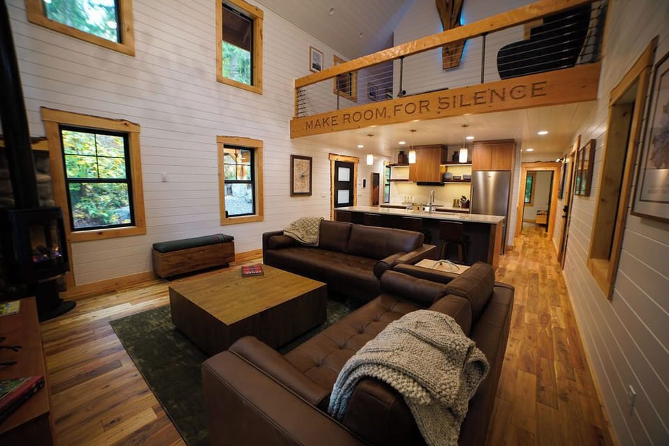 An open-concept living space designed for connection — featuring a gas fireplace, mid-century furnishings, and the signature “Make Room for Silence” beam.