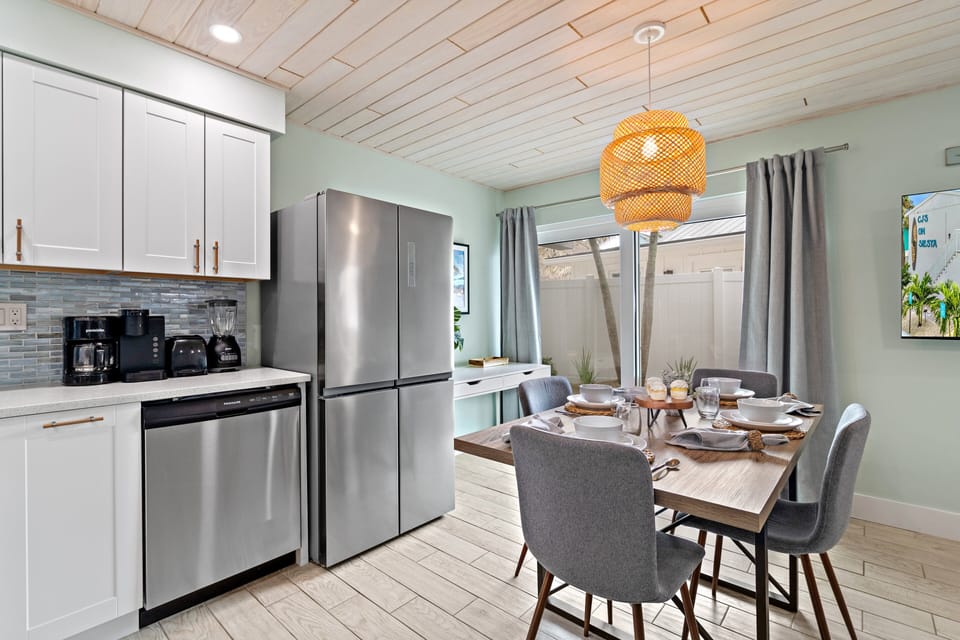 The heart of the home glows with fresh vibes — gather around the dining table or step outside through glass sliders to soak in the sea breeze.