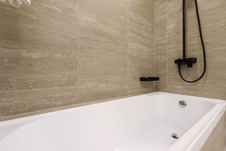 Modern bathtub with beige tiled walls and sleek black shower fixtures.