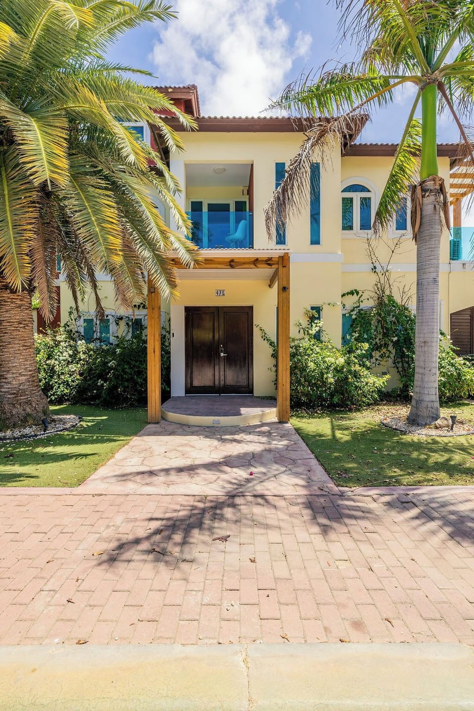 A welcoming two-story tropical villa features a covered entryway and lush palm trees, set in a peaceful residential area.