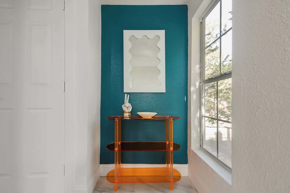 A hallway nook with a teal accent wall, a modern mirror, and an orange console table creates a stylish focal point.