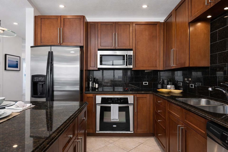 Modern kitchen with granite counters, stainless steel appliances, and sleek wood cabinetry—perfect for cooking, entertaining, and relaxing in style. Ideal for families or couples seeking comfort and convenience near the beach.