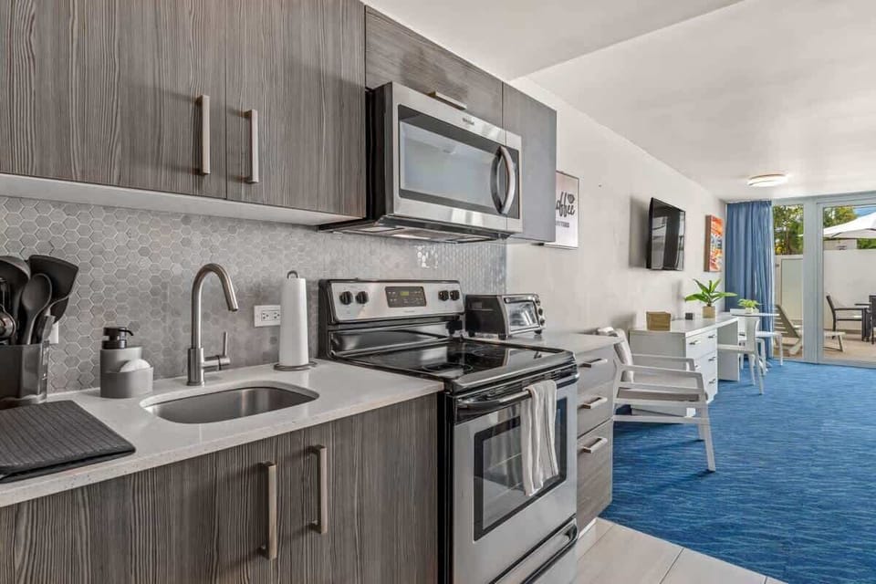 The space features stylish light-colored, wood-grain cabinets and stainless steel appliances, including a microwave and a stove. 