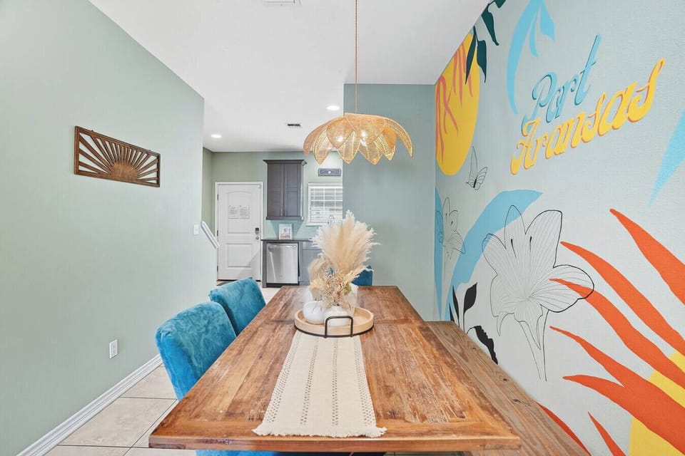Enjoy meals together at the spacious dining table with a vibrant Port Aransas wall design