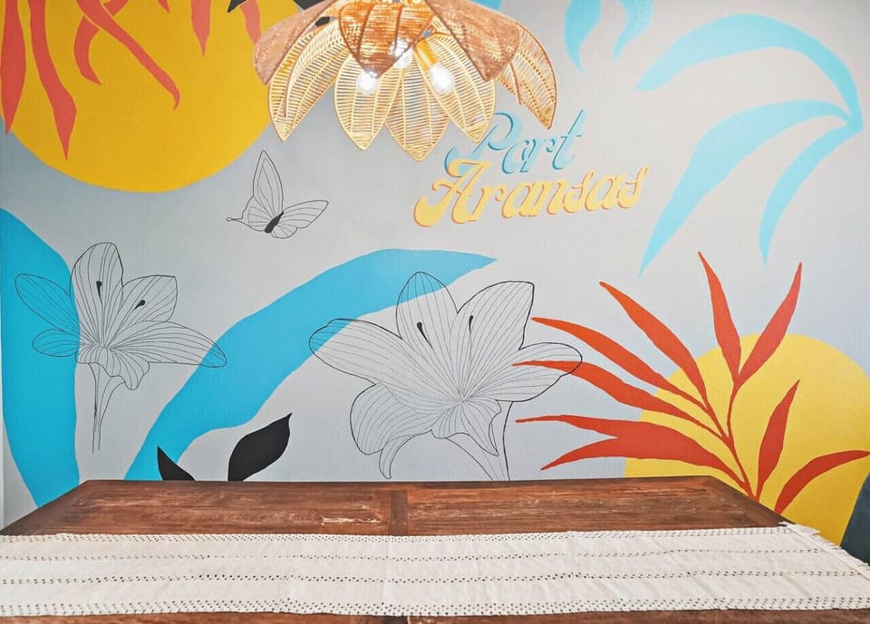 Enjoy meals together at the spacious dining table with a vibrant Port Aransas wall design