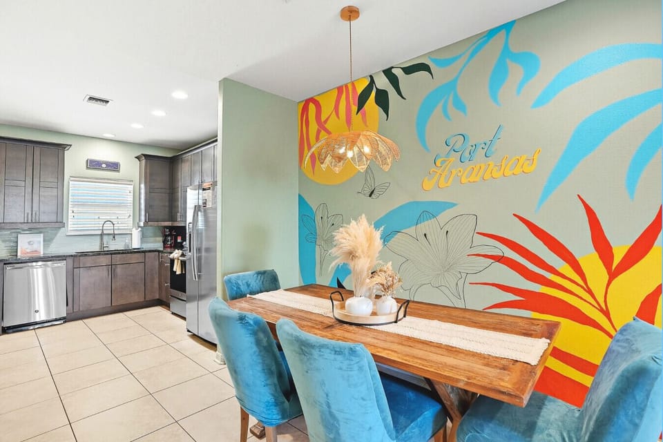 Enjoy meals together at the spacious dining table with a vibrant Port Aransas wall design