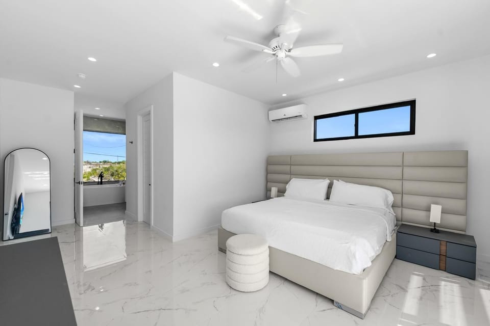 A minimalist white bedroom with a large upholstered headboard.