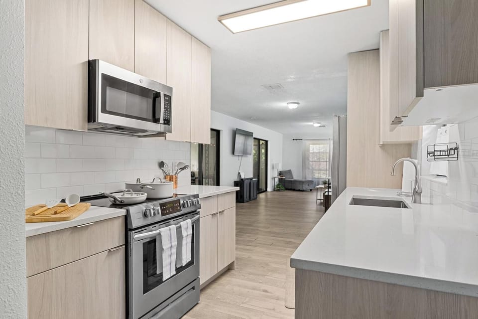 Bright modern kitchen with sleek wood cabinetry, stainless steel appliances, and quartz countertops. Fully equipped for home cooking, seamlessly connected to the open living area for easy entertaining.