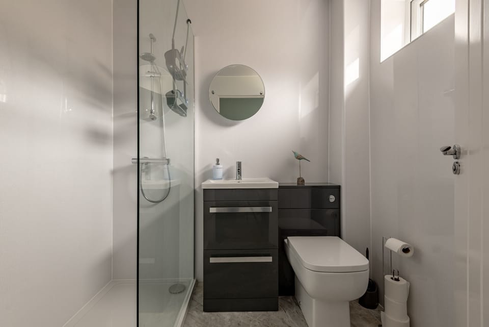 Modern bathroom with walk-in shower, black gloss vanity unit, wall-mounted mirror, and compact toilet.
