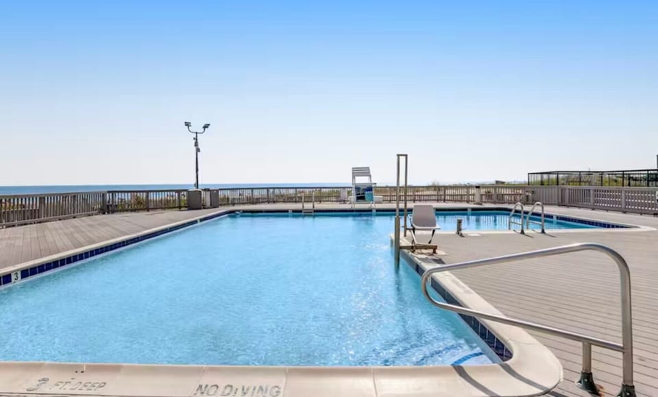 An outdoor swimming pool surrounded by a wooden deck with an ocean view.