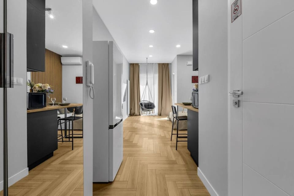 Hallway with Bright Interior – Spacious entry with large mirrors, wood flooring, and direct view into the cozy living space with hanging chair | Book Now with RENTUJEMY.COM