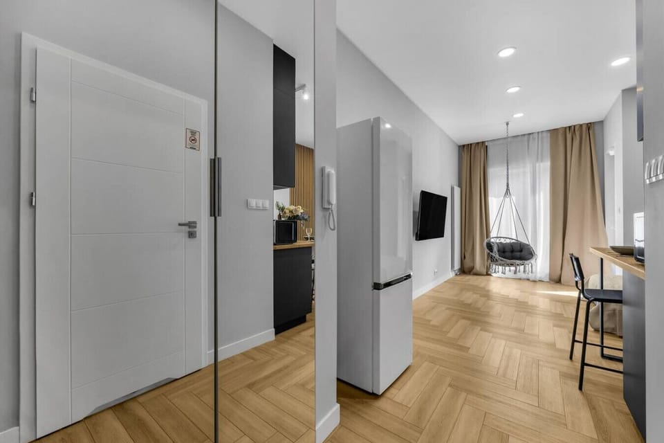 Hallway with Bright Interior – Spacious entry with large mirrors, wood flooring, and direct view into the cozy living space with hanging chair | Book Now with RENTUJEMY.COM