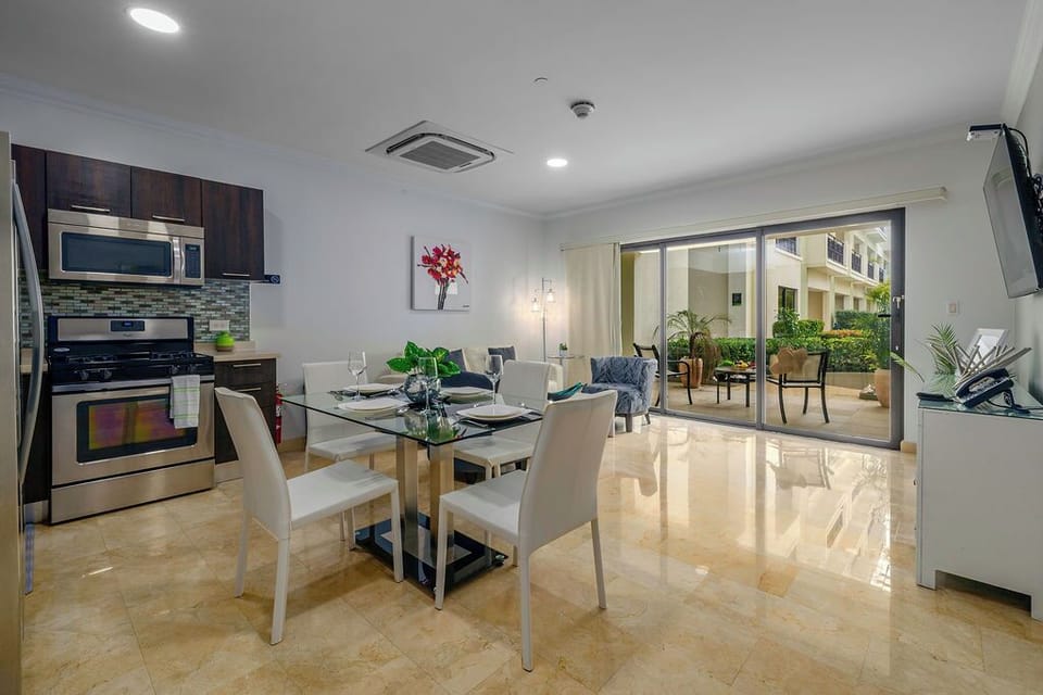 A glass-top dining table paired with chic, white leather-style chairs provides seating for four in a bright, contemporary setting.