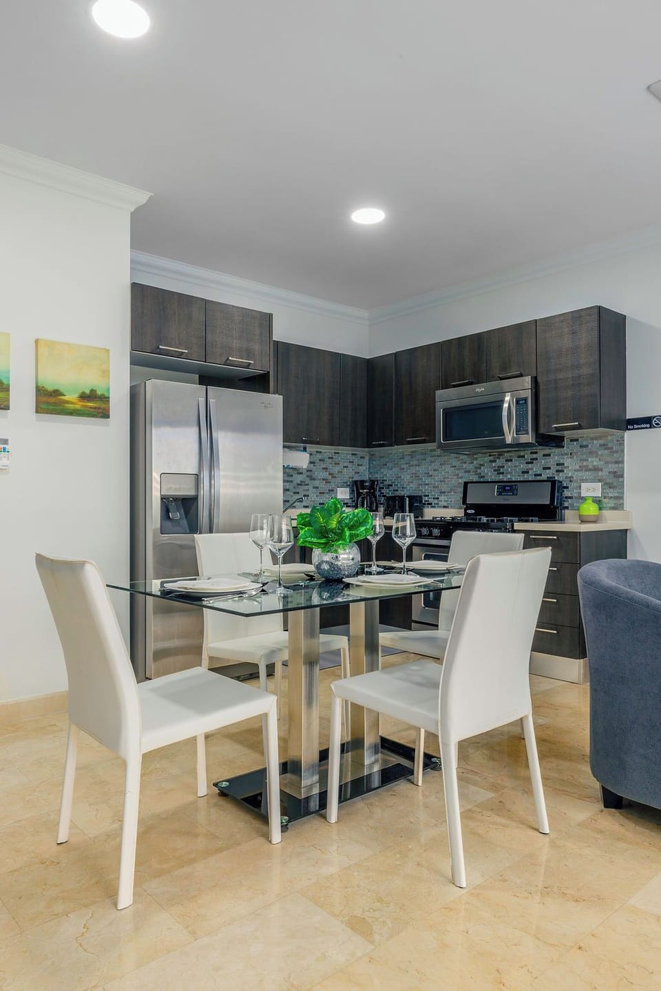 A glass-top dining table paired with chic, white leather-style chairs provides seating for four in a bright, contemporary setting.