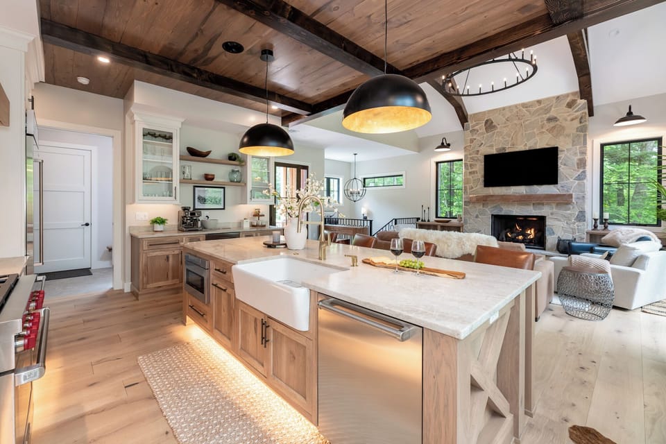Beautiful open kitchen with a large island, farmhouse sink, and modern appliances. Overlooks the cozy living area with vaulted wood ceilings and a stone fireplace, perfect for cooking, entertaining, and relaxing together.