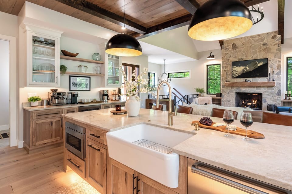 Beautiful open kitchen with a large island, farmhouse sink, and modern appliances. Overlooks the cozy living area with vaulted wood ceilings and a stone fireplace, perfect for cooking, entertaining, and relaxing together.