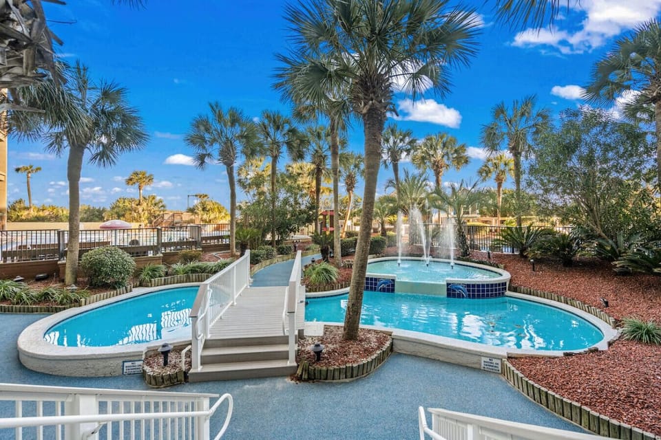 Tropically themed fountains and resort grounds at Beach Cove Resort create a relaxing coastal oasis. Palm trees, flowing water features, and vibrant landscaping enhance the true resort-style vacation experience.