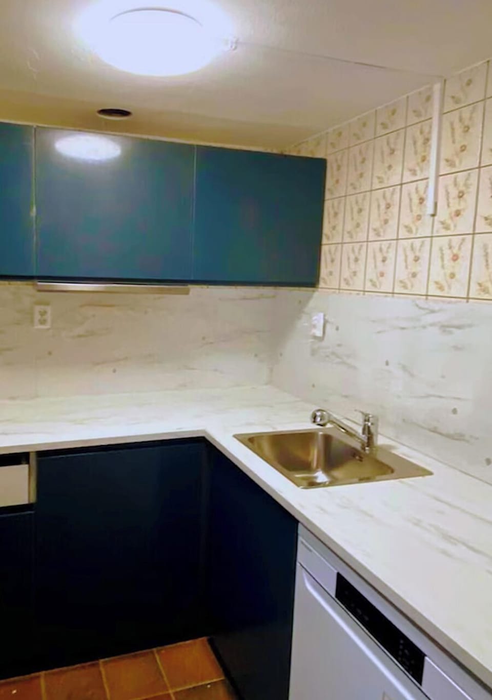 This compact kitchen features a sleek design with dark blue cabinets, a modern stainless steel sink, and light marble countertops—perfect for simple meal prep.