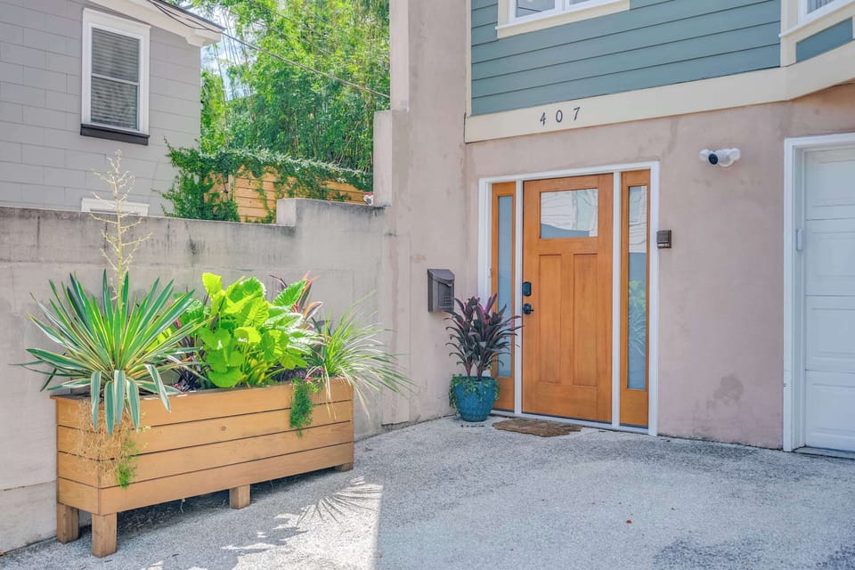 A warm wooden entry door welcomes you beside a raised plant bed filled with vibrant green plants for a fresh first impression!