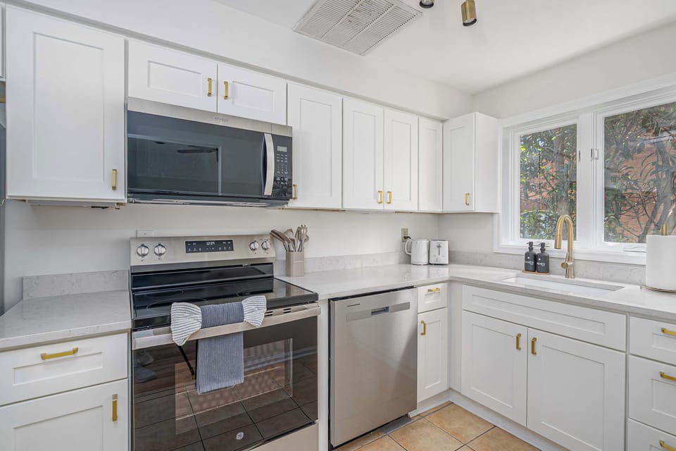 This elegant, fully-stocked kitchen features crisp white cabinets accented with stylish gold handles for a modern, polished look!